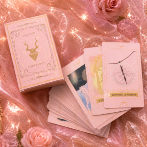 "A stack of pink tarot cards leaning against their matching tuck box. The cards feature a minimalist celestial design with gold-toned illustrations on a soft blush-pink background, created by an independent artist.